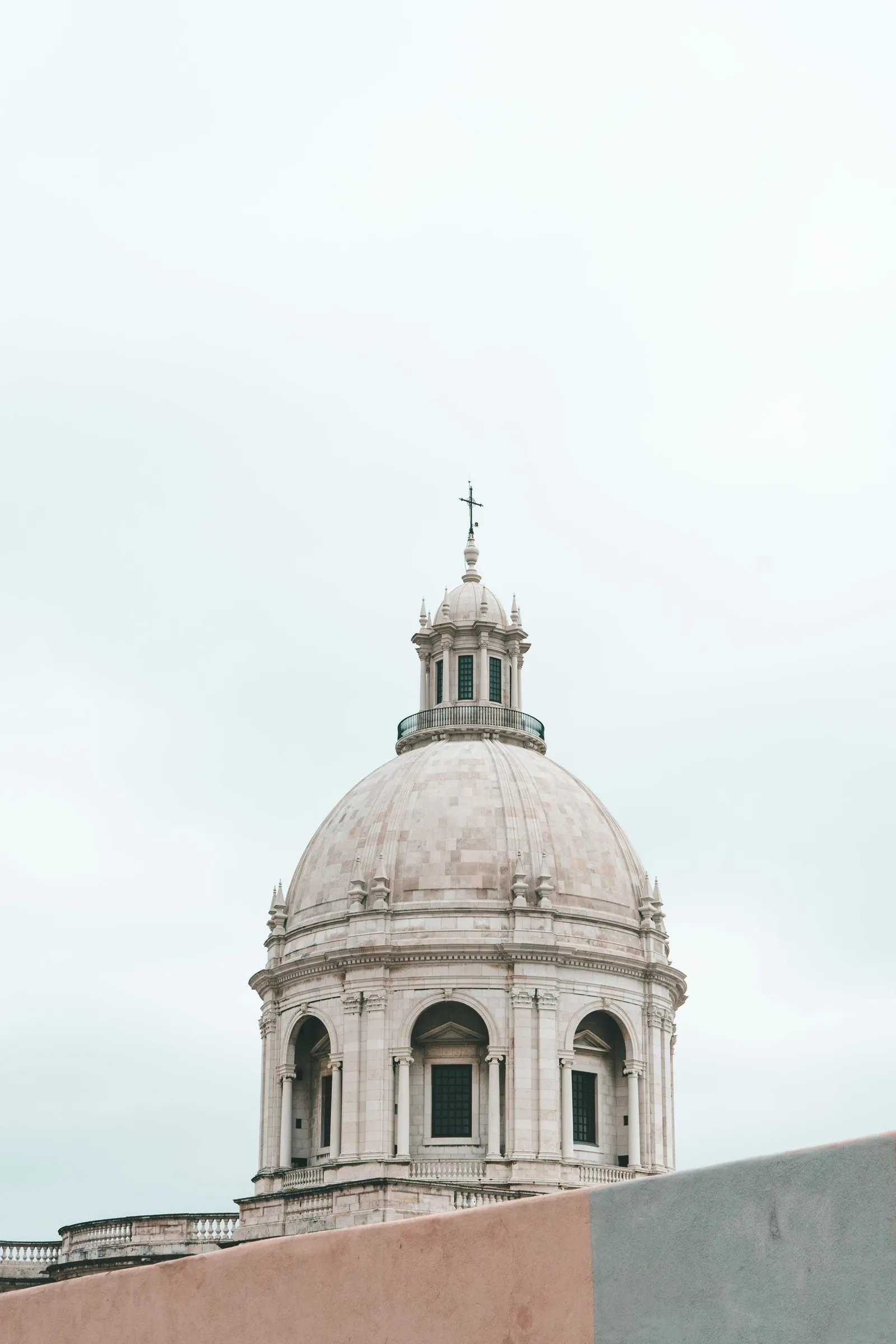 Dôme monumental en pierre blanche du Panthéon National de Lisbonne, surmonté d'une croix, avec ses arches et colonnes baroques se détachant sur un ciel nuageux