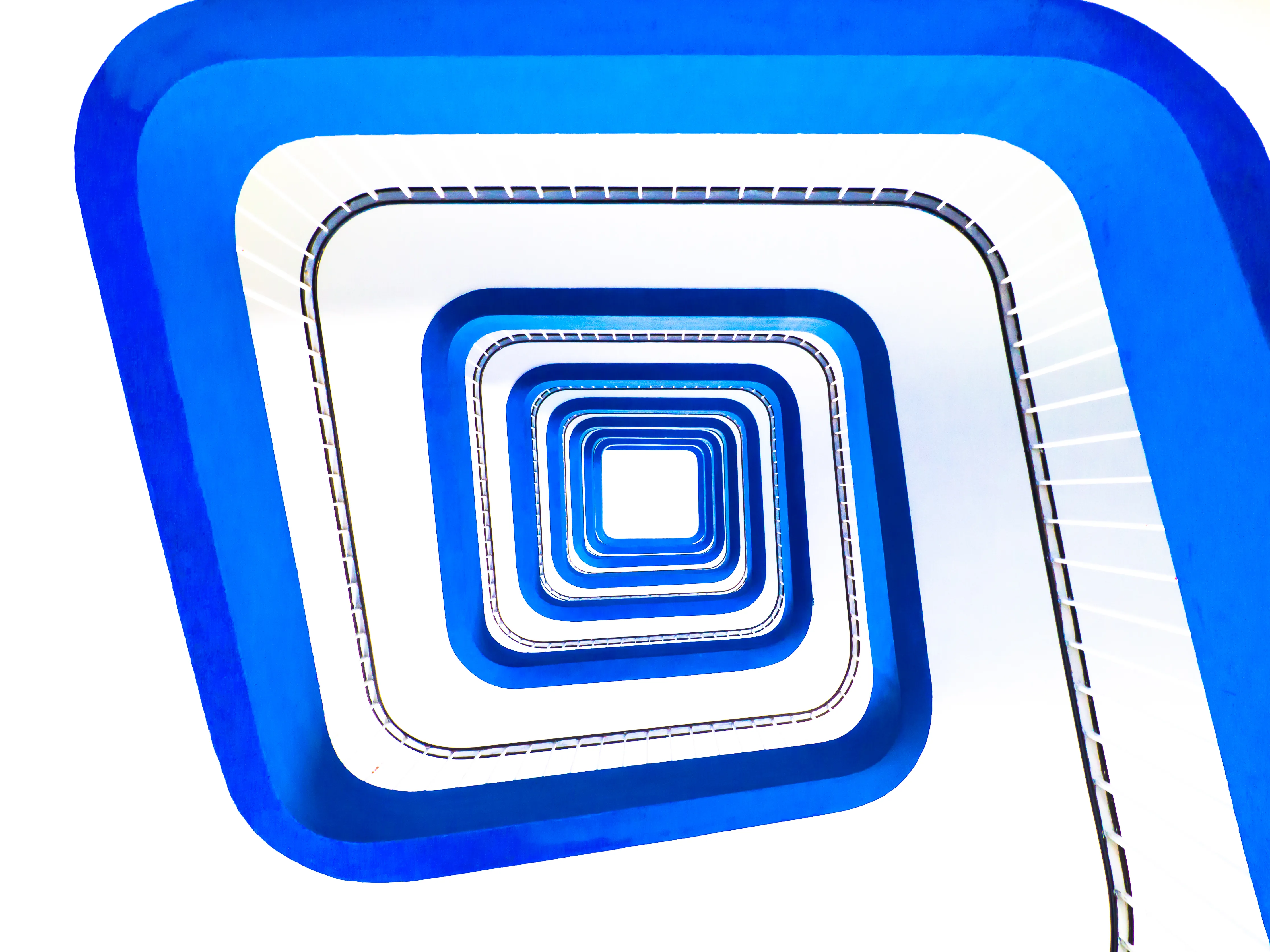 Escaliers en spirale bleu électrique avec effet de profondeur et de mouvement, vue depuis le bas. Design géométrique et moderne, jeu de lumière sur les bords blancs et bleus.